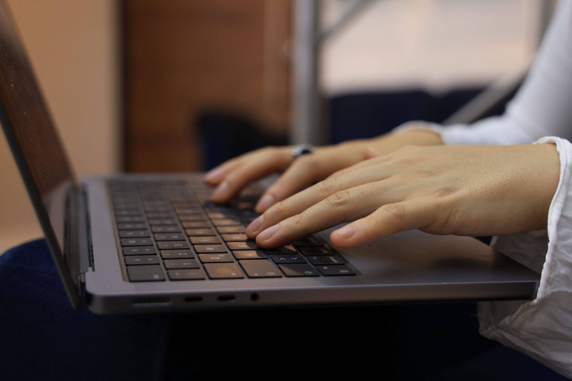 Hands typing on a laptop keyboard at a home desk in the evening.
